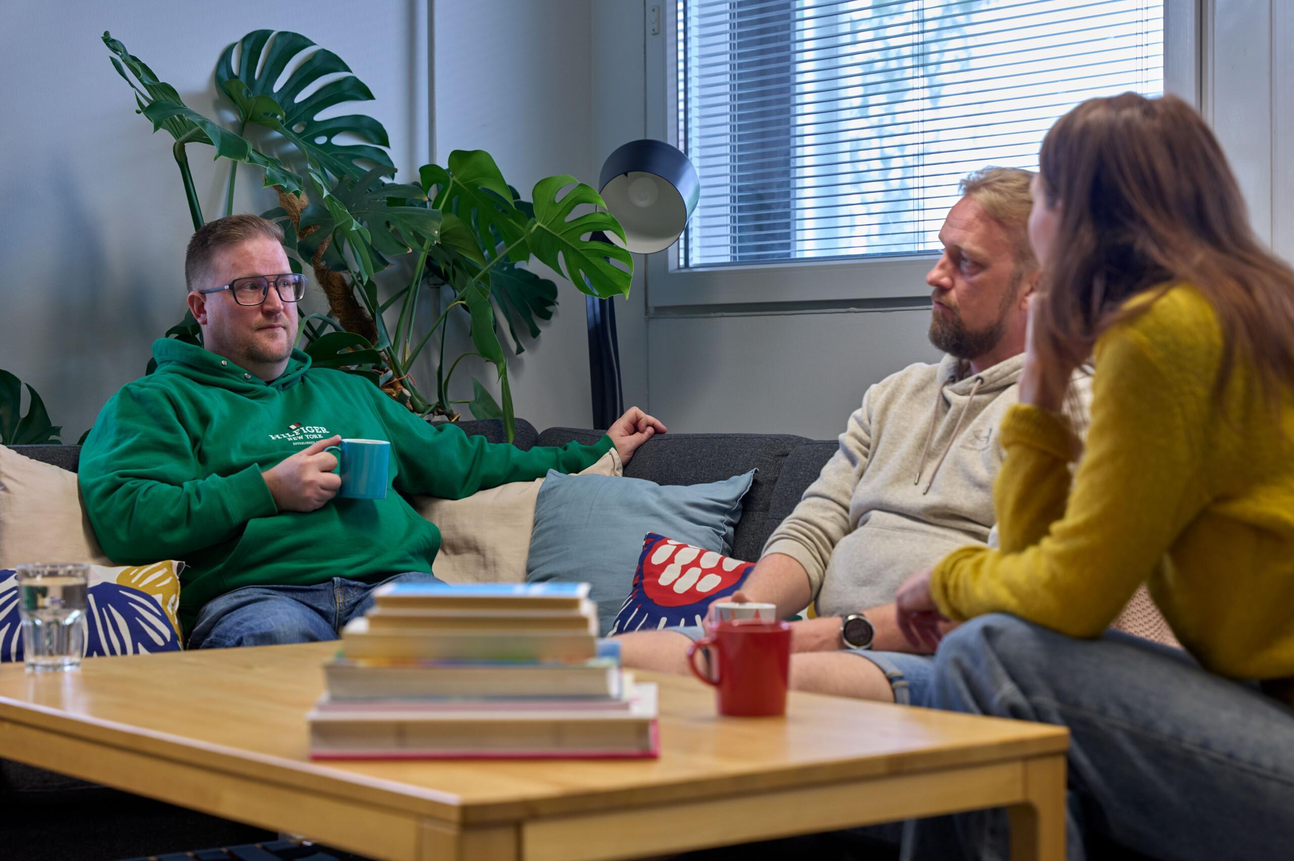 Kolme henkilöä istuu sohvalla ja keskustelee